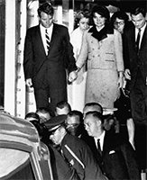 Jane and Bobby holding hands as an empty casket is unloaded at Andrews Air Force Base. 